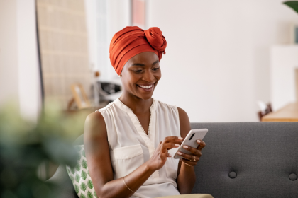 A woman is smiling and looking at her phone at home while learning about ahamo phone plans