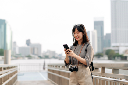 A woman with a camera around her neck looks at her phone while standing on a Tokyo bridge